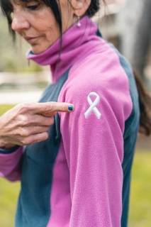 Mid adult woman pointing to an embroidered cancer awareness ribbon with her finger on her sweatshirt. Vertical shot