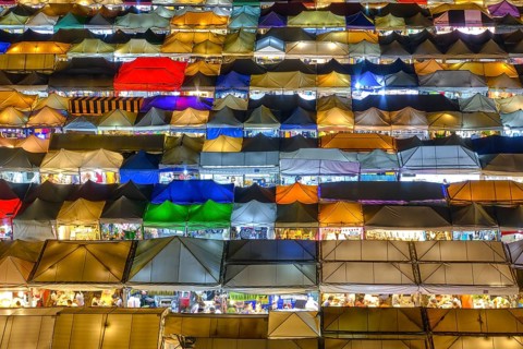Close-up view of rows of colorful outdoor market tents and food stalls at night. Fairs