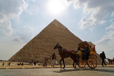Two-wheeled horse-drawn carriage passes in front of a pyramid