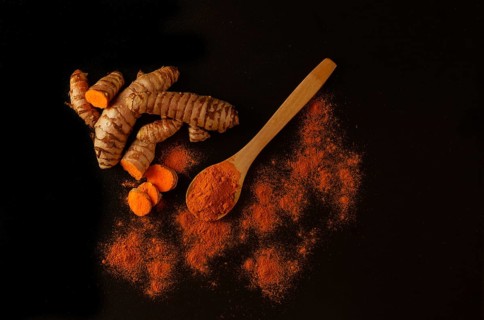 Fresh turmeric root and ground turmeric in a wooden spoon isolated on black background and copy space