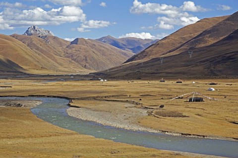 Tibetan nomadic tents with prayer flags and herd of yaks grazing along the Sichuan-Tibet Highway