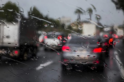 Trucks overtaking cars on highway during heavy rain shower seen from inside of vehicle with big raindrops on windscreen
