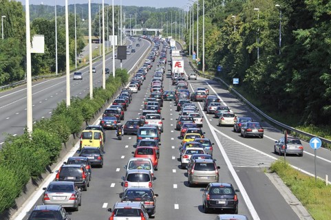Cars and trucks queueing in highway lanes at approach slip road during traffic jam on motorway during summer holidays