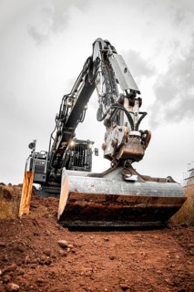 Black Liebherr crawler excavator excavating earth for house construction on building site