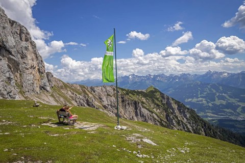 Young couple sitting on bench next to green flag of the Austrian Alpine Club