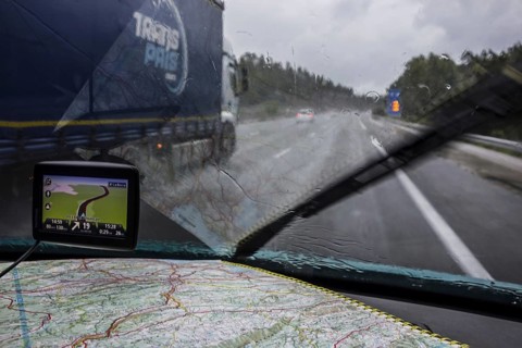 Speeding truck overtaking car on highway during heavy rain shower seen from inside of vehicle with GPS and road map on dashboard