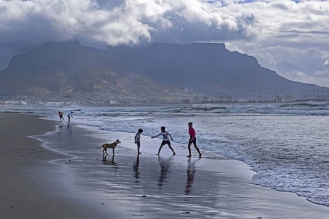 Rain clouds over Table Mountain and children playing on sandy Sunset Beach near Cape Town