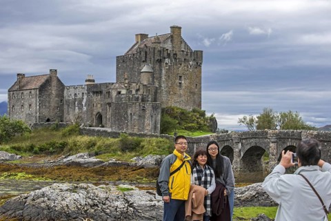 Asian tourists posing in front of Eilean Donan Castle in Loch Duich