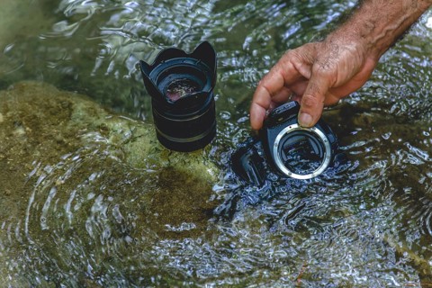 A man cleans the sensor of his reflex camera in the water of a river by flooding it from the inside