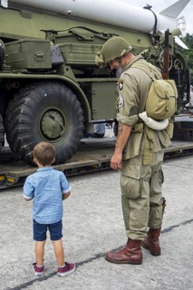 Little boy and WW2 reenactor in US soldier outfit looking at missile truck at World War Two militaria fair