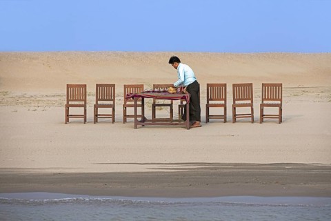 Burmese servant preparing dinner and setting the table for tourists at sunset along the Irrawaddy River