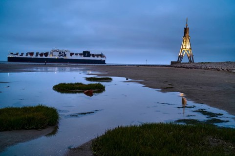 Kugelbake illuminated with cargo ship at dusk
