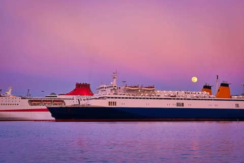 Two ferries moored parallel by pier at colorful sunset during moonrise. Popular transportation for island hopping in Mediterranean sea