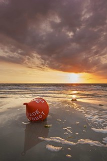 Seascape showing orange buoy on the beach at low tide and sunset over the Wadden Sea