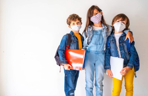Three children with face masks ready to go back to school. New normality