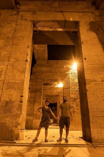A couple of tourists between the columns at night of the temple of Kom Ombo in traditional dress