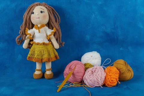 Amigurumi doll handmade on a blue background with the yarns used for its elaboration