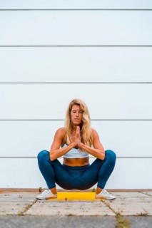 Yoga with blonde caucasian girl doing exercise on a yellow mat with white wall in the background