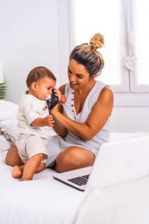 Young Caucasian mother with her son in the room on top of the bed. Mother teleworking and caring for her child