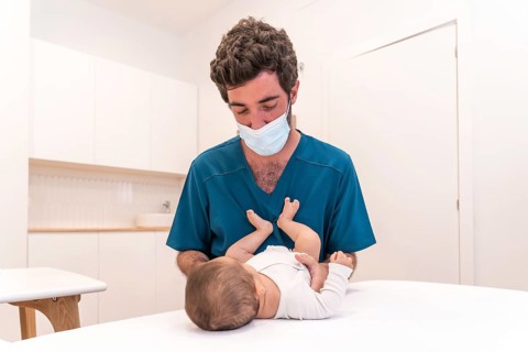 Portrait of a young doctor checking up a baby lying down on stretcher in a clinic