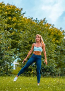 Fitness session with a young blonde Caucasian woman exercising on the street with a blue maya on her feet and a white short shirt. Performing side jumps