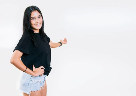 Happy young girl welcoming you isolated. Smiling latin girl pointing back presenting a product. Latin girl pointing a promotion with her palm