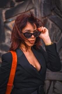 Brunette girl in the city with sunglasses and red bag on a stone wall looking at the camera