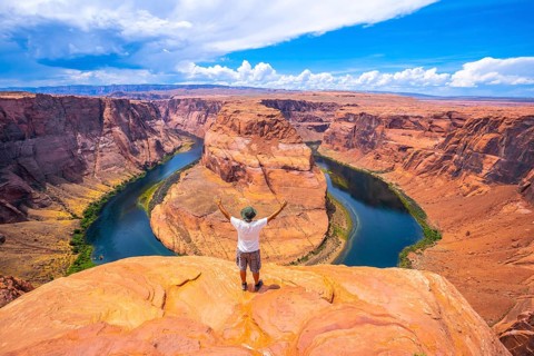 A young man in a white shirt and a green hat at Horseshoe Bend and the Colorado River in the background