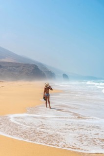 A young tourist with a hat walking alone on the Cofete beach of the Jandia natural park