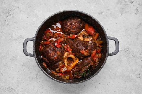Top view of prepared beef ossobuco with chopped vegetables in a casserole