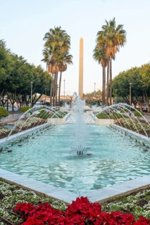 Water fountain and flowers next to palm trees on Las Belen street of Rambla de Almeria at sunset