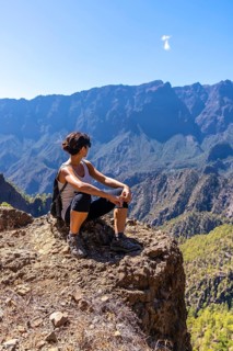 A young woman resting after trekking on top of La Cumbrecita sitting in the natural viewpoint looking at the mountains of the Caldera de Taburiente