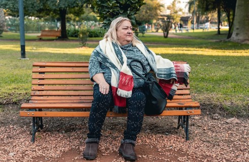 Senior serious woman waits for someone sitting on a bench at a public park