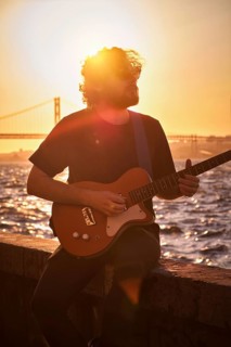 Hipster street musician in black playing electric guitar in the street on sunset