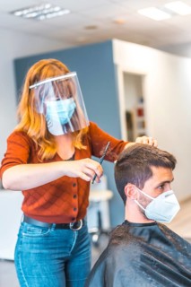 Hairdressers after the Coronavirus pandemic. Hairdresser with face mask and protective screen
