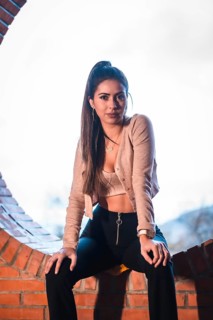 Portrait of a Caucasian brunette model sitting in the city with a beautiful ponytail and a pink sweater. Street style fashion