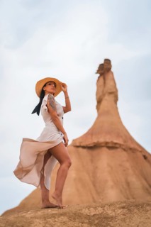 Brunette Caucasian model with a white dress and a straw hat in the Castildetierra of the Bardenas Reales desert