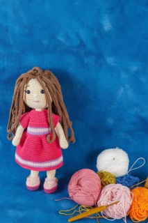 Amigurumi doll handmade on a blue background with the yarns used for its elaboration