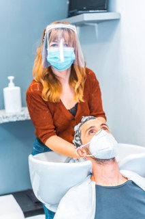 Hairdressers after the Coronavirus pandemic. Caucasian hairdresser with face mask and protective screen