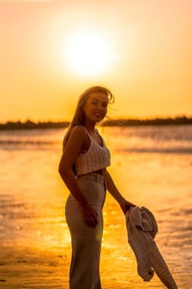 Summer lifestyle. A young blonde Caucasian woman in a white short wool sweater on a beach sunset. With eyes closed and enjoying the sea wind