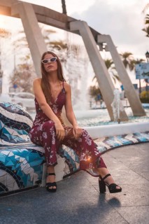 Portrait of a young brunette in a maroon floral dress enjoying the summer in the golden hour in a city fountain