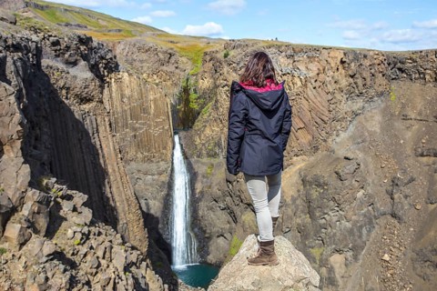 A young woman looking at the waterfall above Hengifoss from above. Iceland