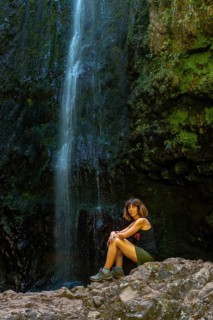 A young woman at the waterfall at the end of the waterfall trail at Levada do Caldeirao Verde