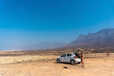 A young girl with the rental car on the Cofete beach of the Jandia natural park