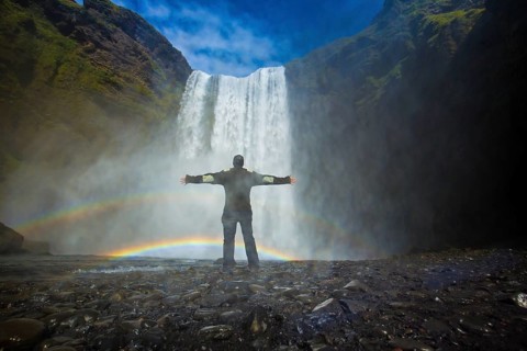 A tourist with open arms at the bottom of the Skogafoss waterfall in the golden circle