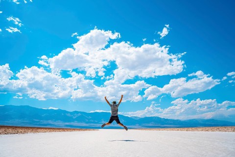 A young man jumping with a blue shirt on the white salt of Badwater Basin