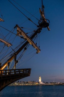 Old ship on the promenade of Muelle Uno in the Malagaport of the city of Malaga and in the background La Farola de Malaga