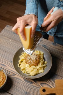 High angle view of female hands grating parmesan cheese into pasta