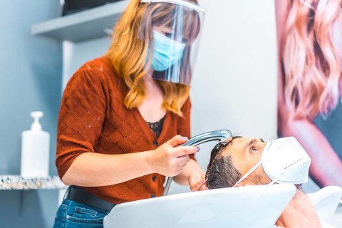 Reopening of hairdressing salons after the Coronavirus pandemic. Hairdresser with face mask and protective screen