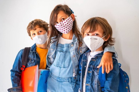 Three children with face masks ready to go back to school. New normality